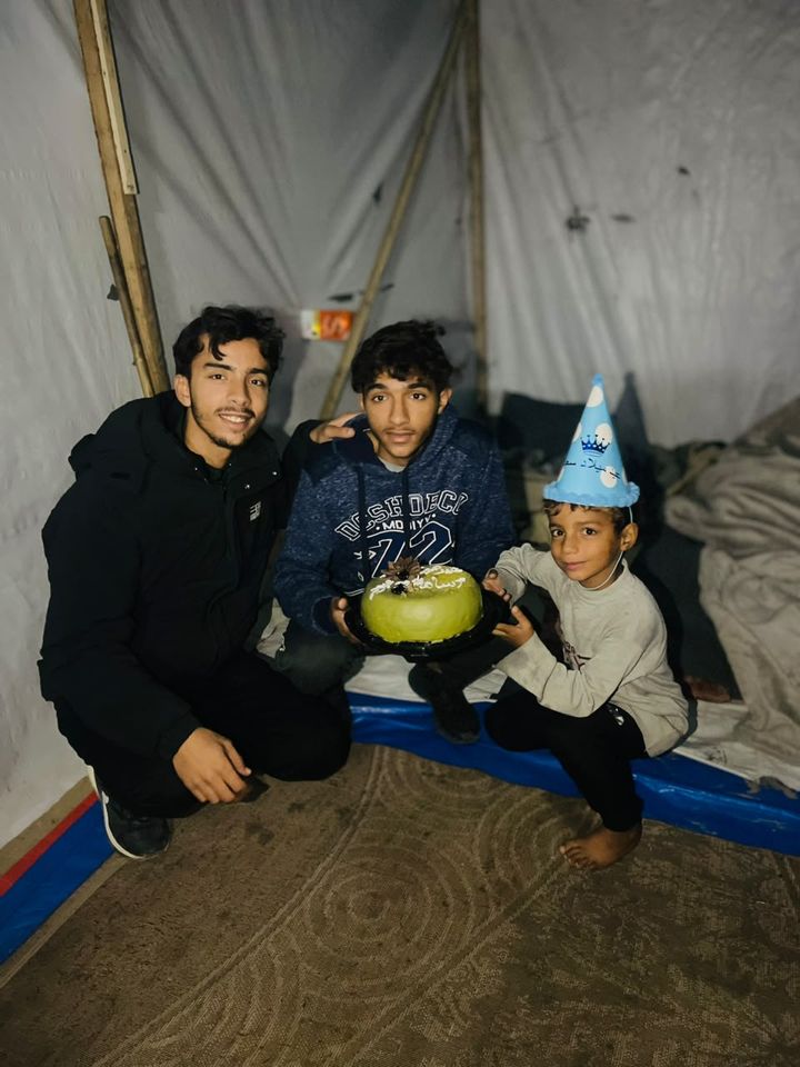 Family members gathered around a birthday cake in a tent
