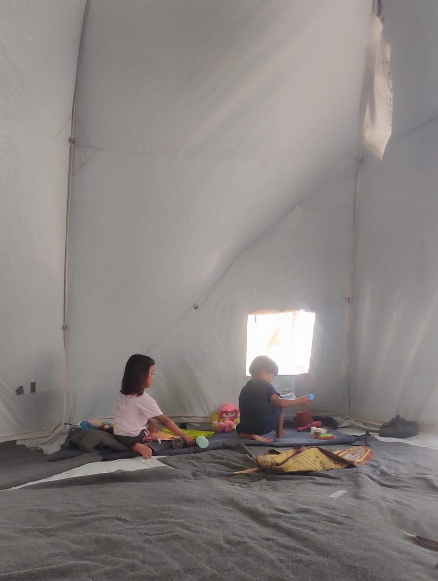Noor's children studying on the ground, using notebooks brought to the tent