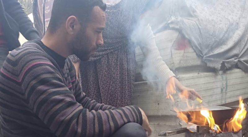 A man and his mother preparing food over a fire at a shelter