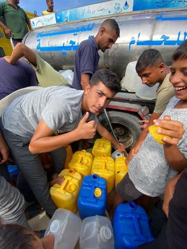 Young men gathered around a water tanker in Gaza, filling containers