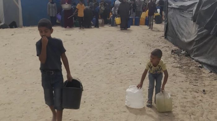 Two of Ziad's children carrying water containers through the camp